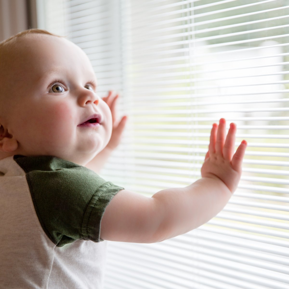 Baby leaning on a window with Blink enclosed blinds